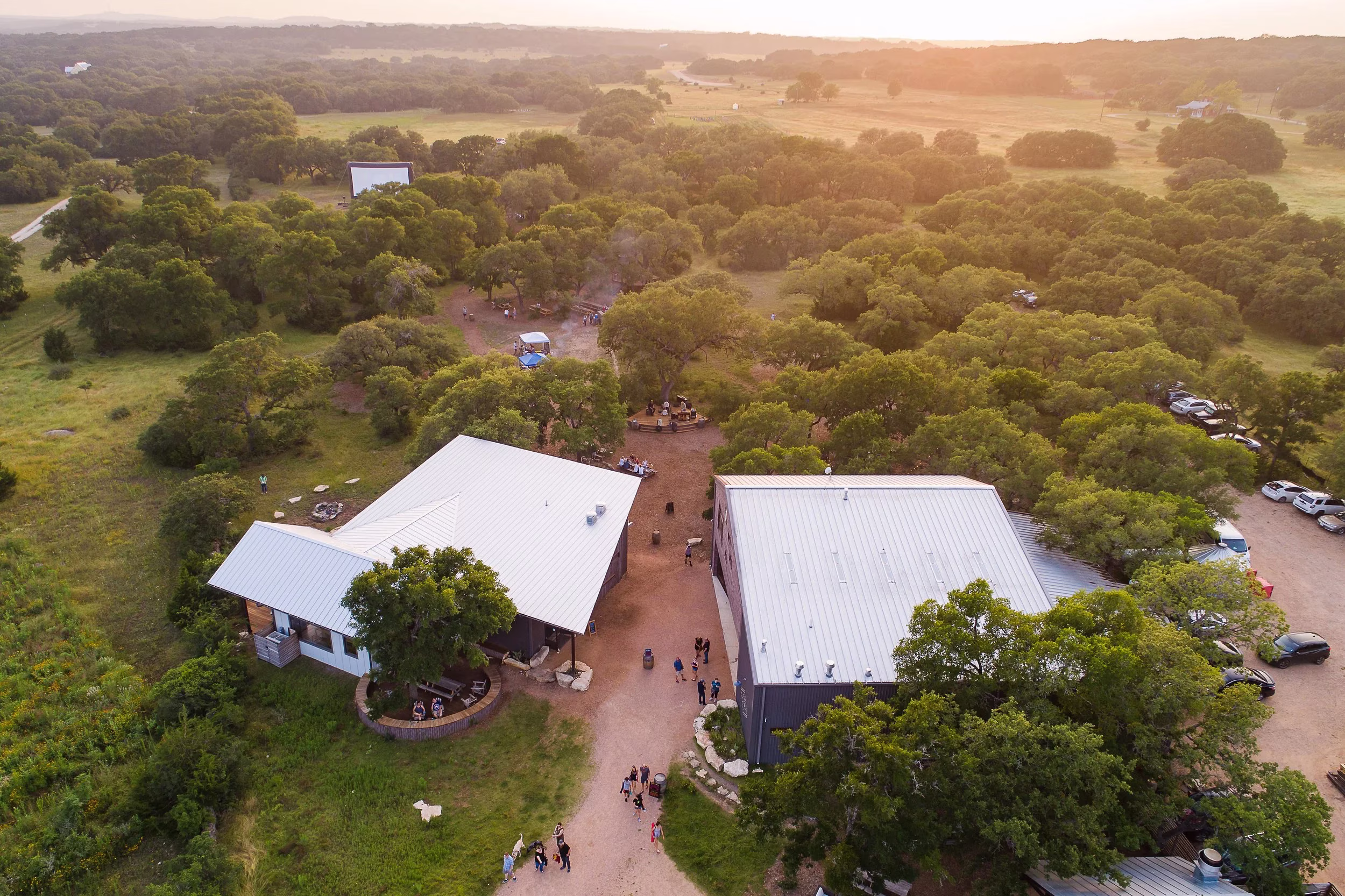 Overhead view of buildings, people, and a large outdoor screen in woods.