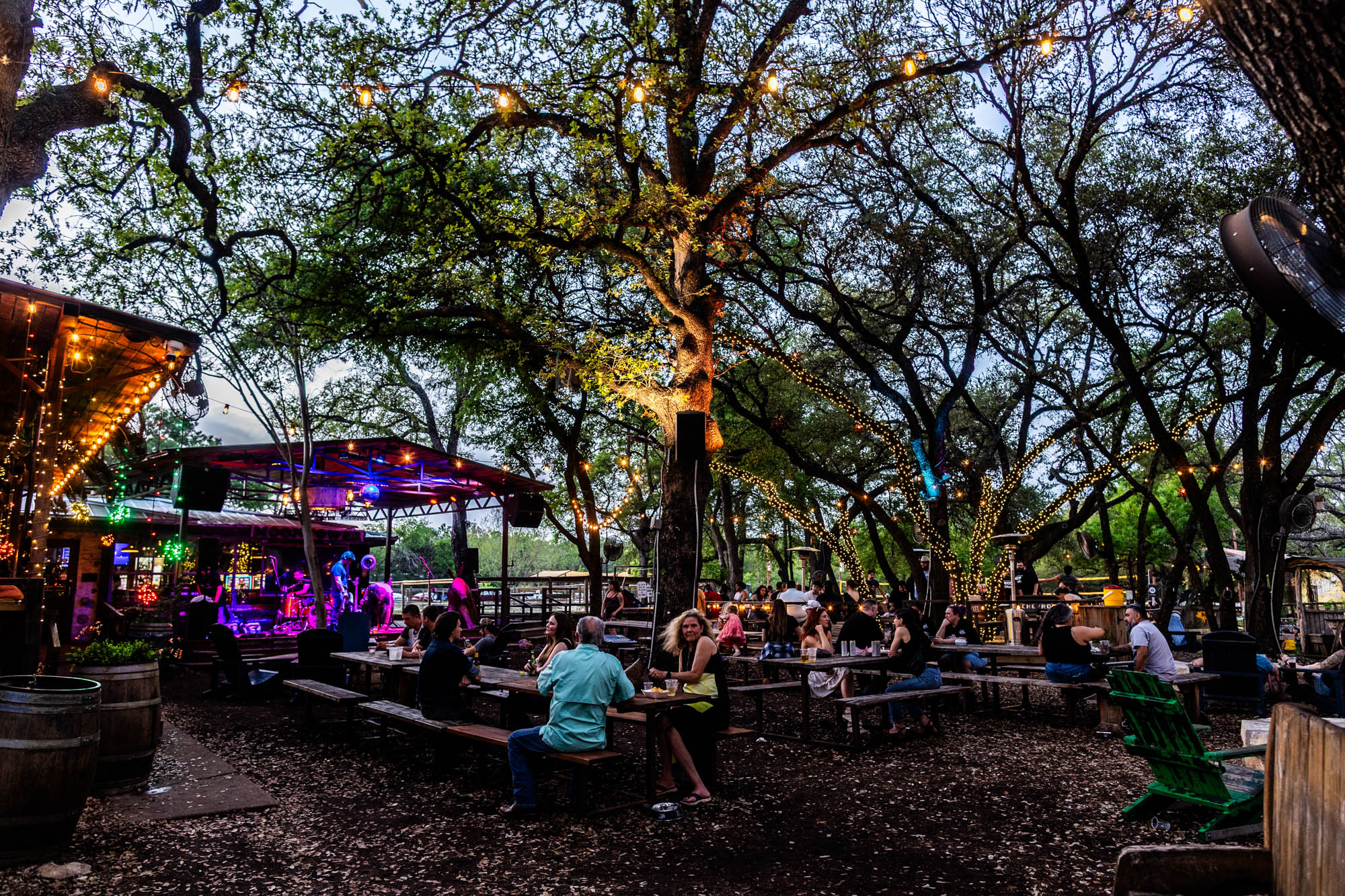 Outdoor bar with live music, people, and trees covered in lights.