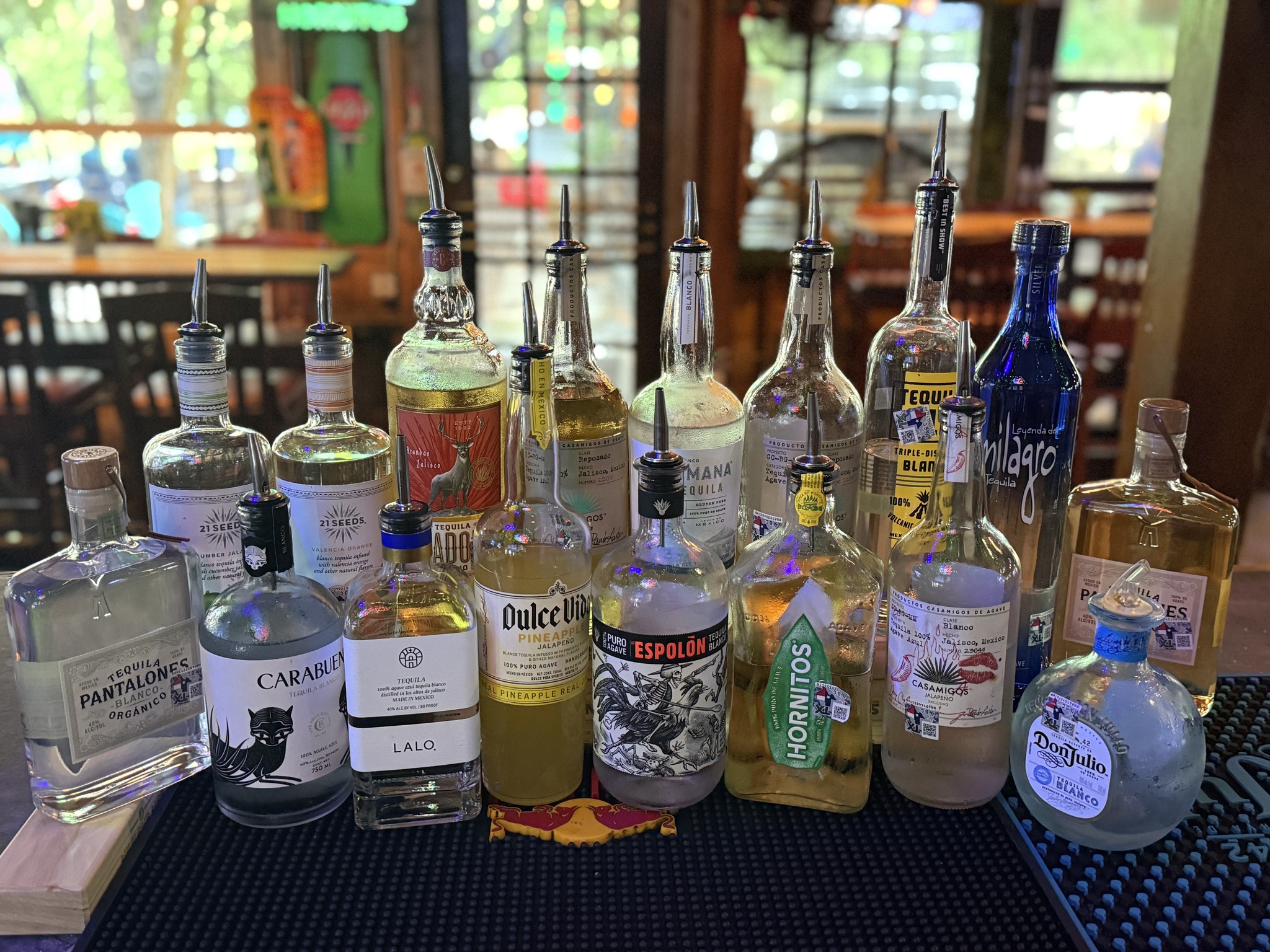 Numerous tequila bottles with pour spouts displayed on a bar counter.