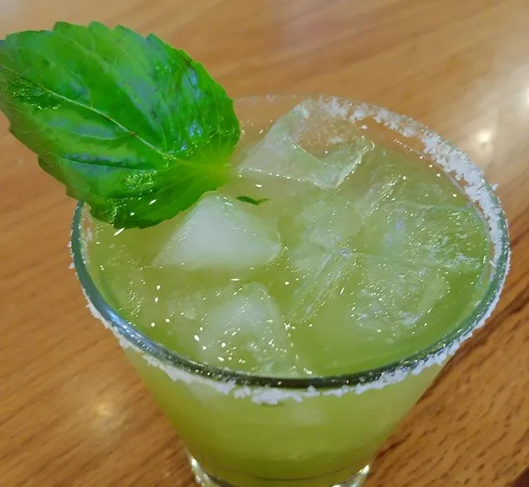 Vibrant green cocktail with ice, leaf garnish, and sugared rim.
