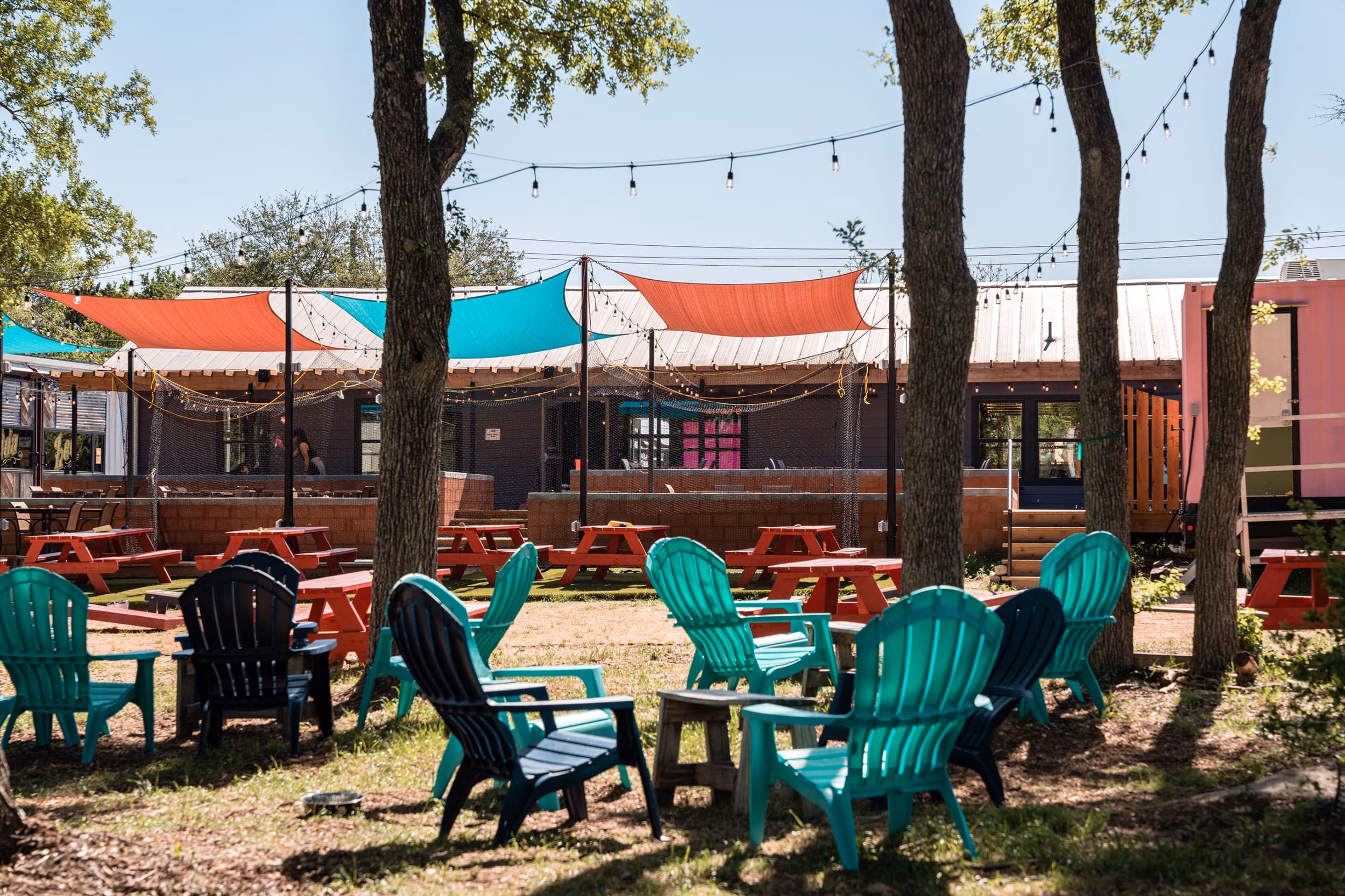 Outdoor patio with colorful shade sails, Adirondack chairs, and picnic tables.