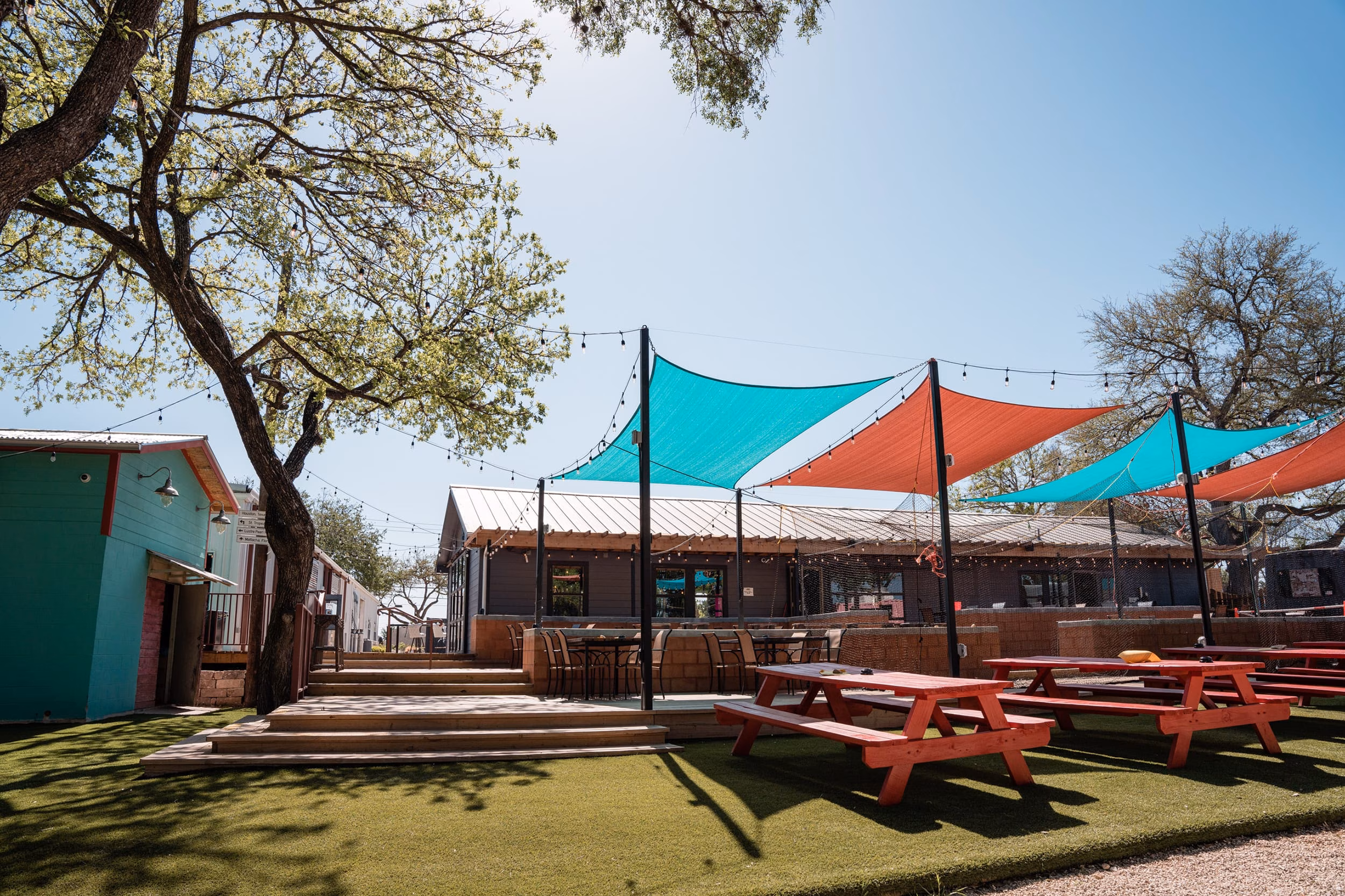 Outdoor patio with red picnic tables, teal and red shade sails.