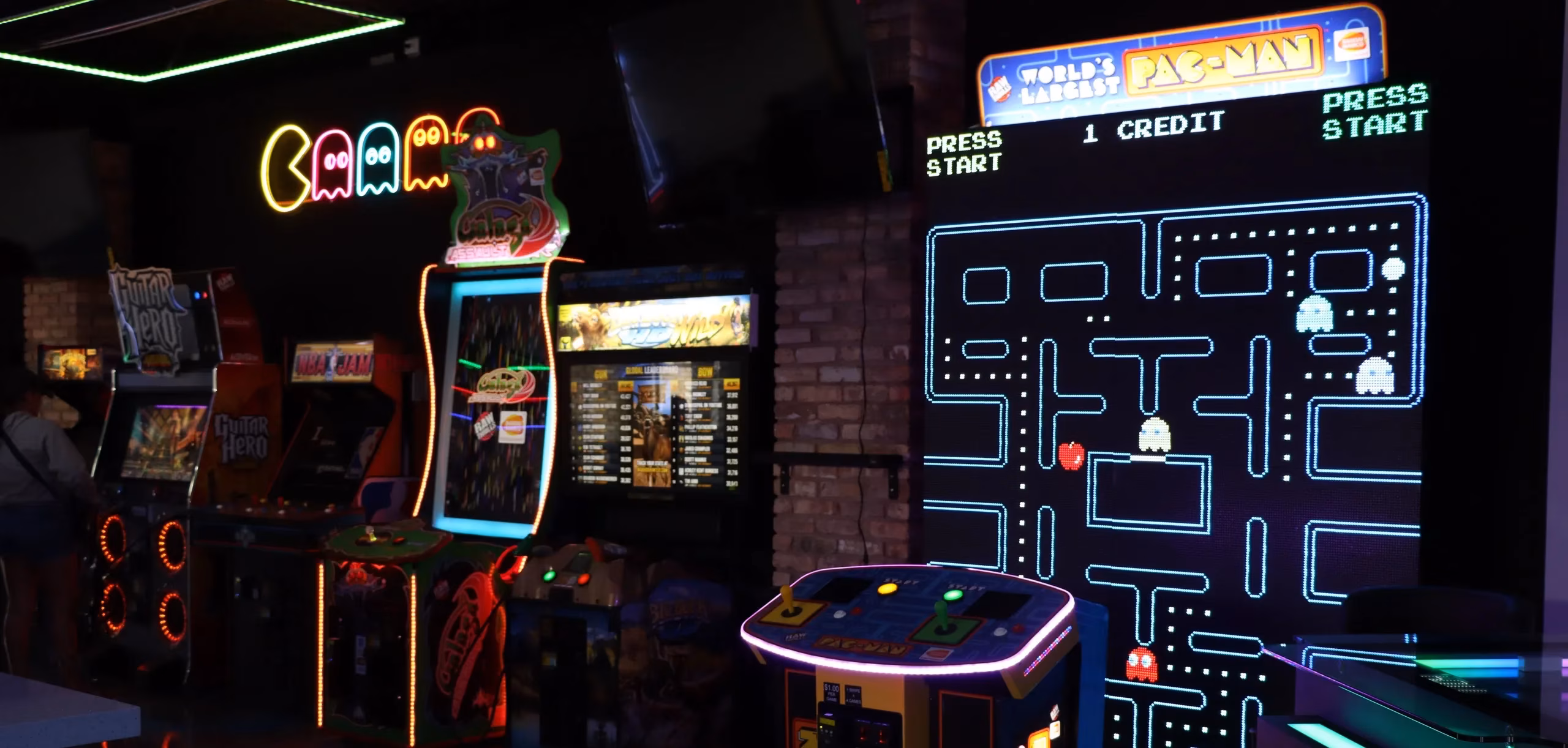 Neon-lit arcade with a large Pac-Man game and multiple machines.