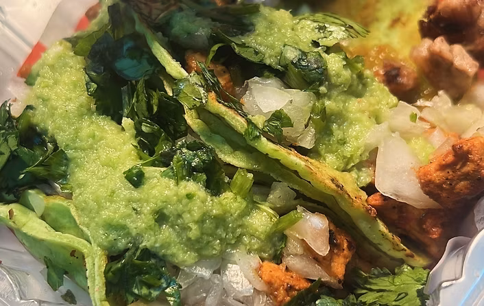 Green tortillas topped with meat, cilantro, onions, and green sauce.