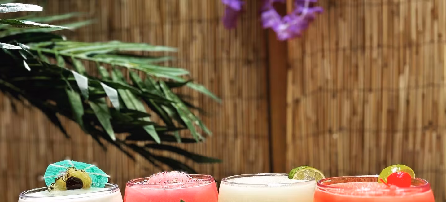 Four colorful, garnished drinks set against a bamboo and leaf background.
