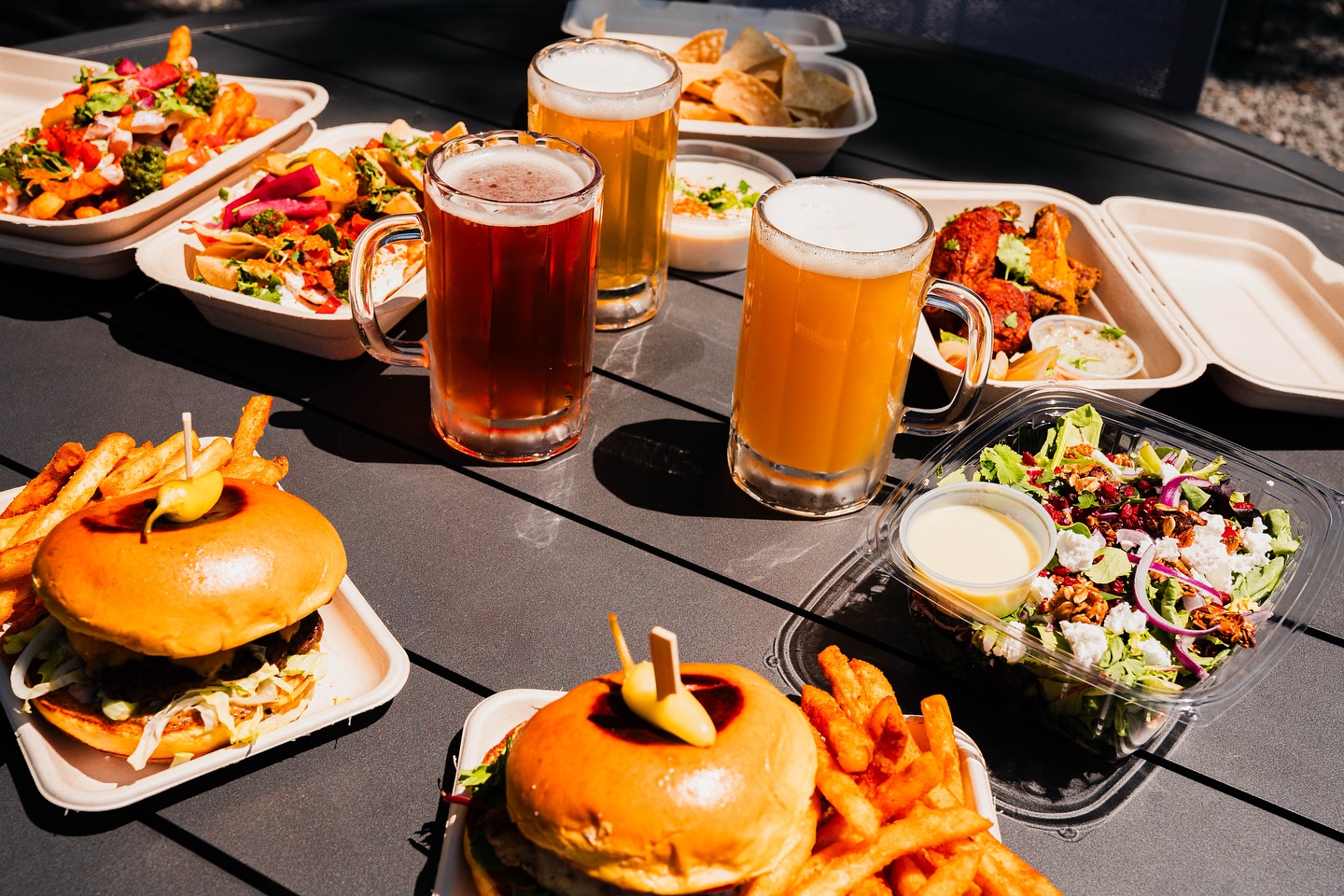 Various takeout food dishes and three mugs of beer on a table.