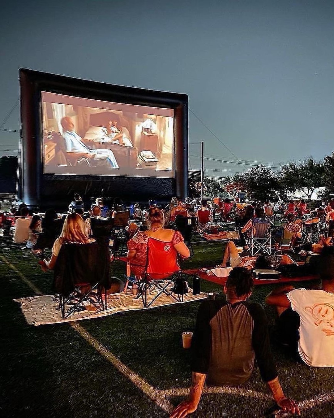 People watching an outdoor movie on a large inflatable screen at night.