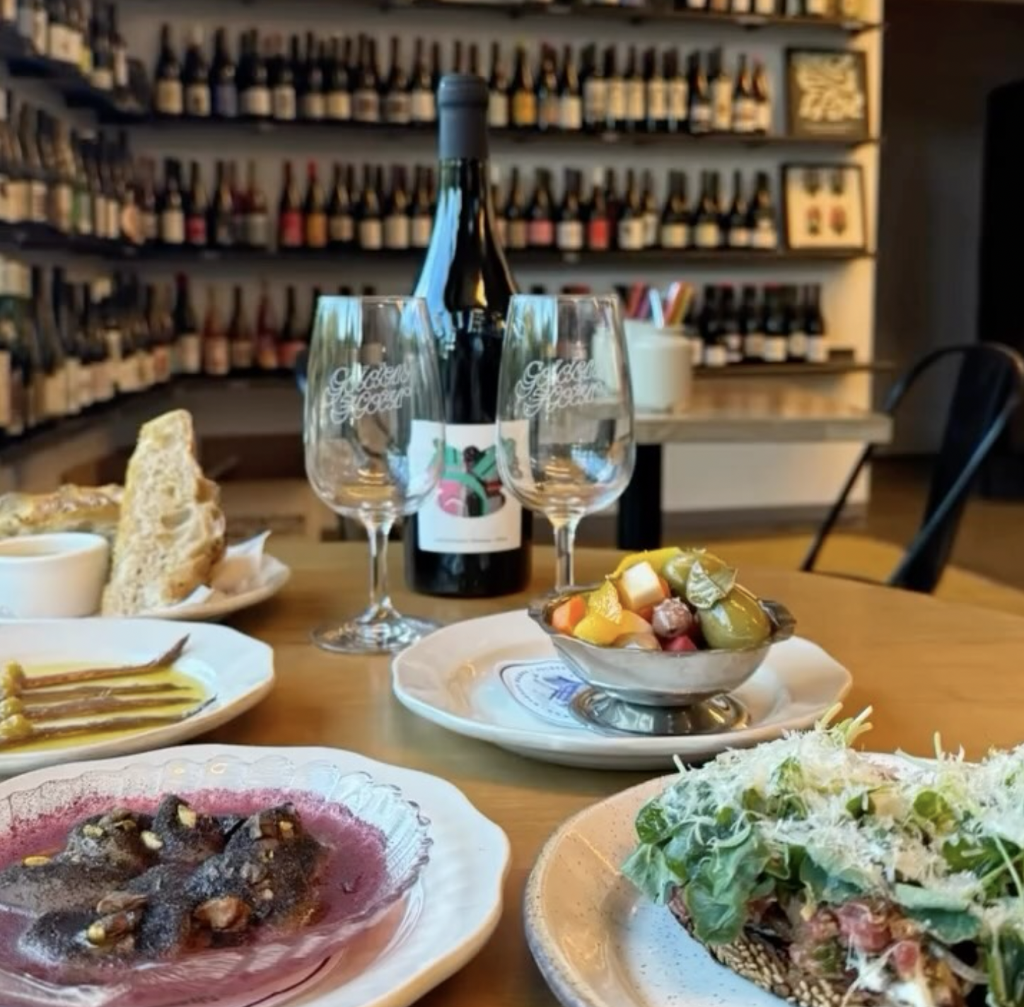 Wine bottle, branded glasses, and small plates on a table.