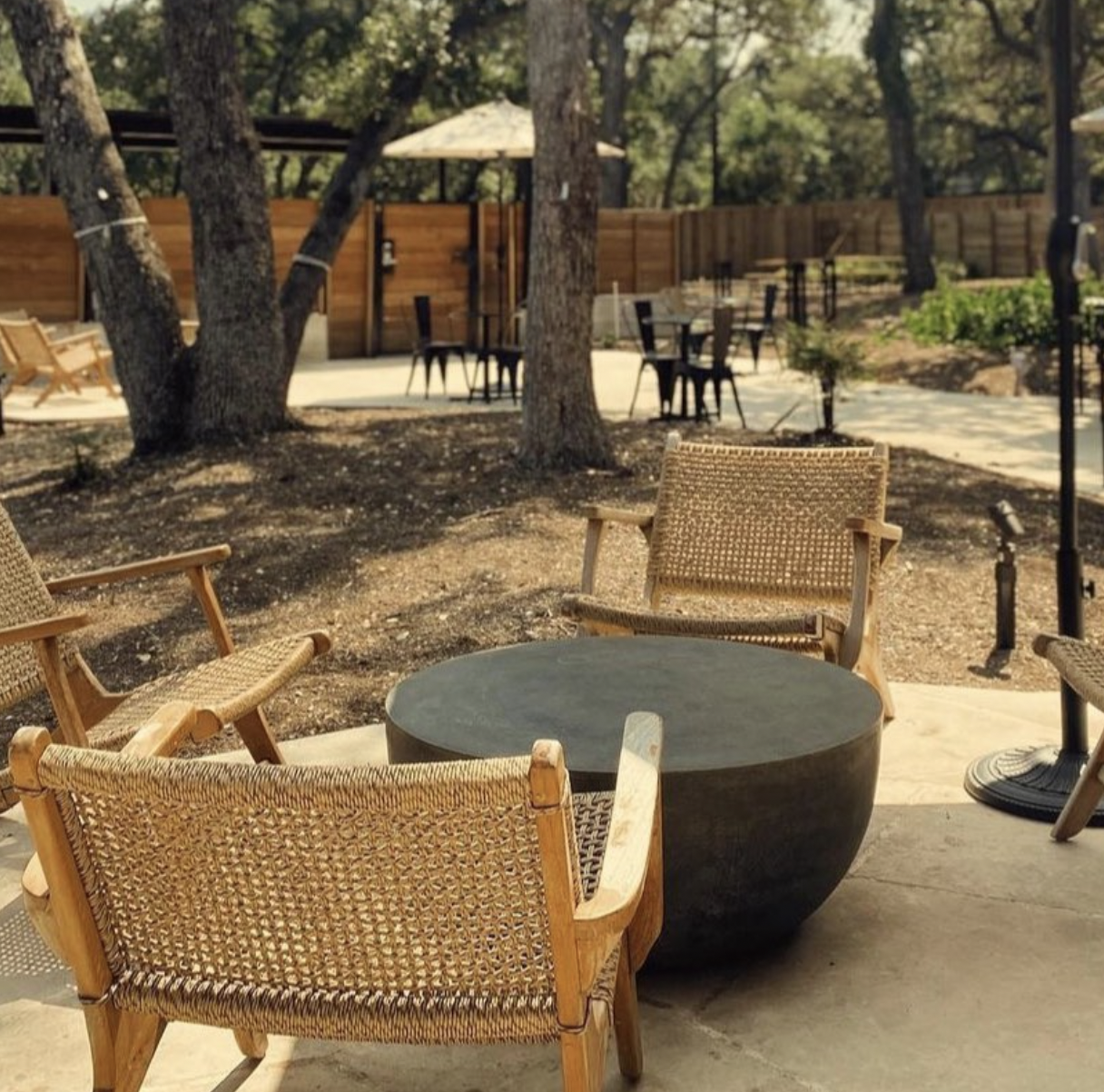 Outdoor patio with woven chairs, concrete table, trees, and fenced background.