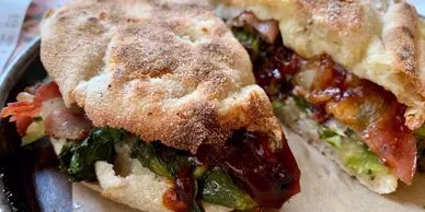 Two halves of a flatbread sandwich with bacon, greens, and dark sauce.