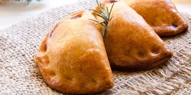 Three golden-brown turnovers on a textured cloth, one garnished with rosemary.