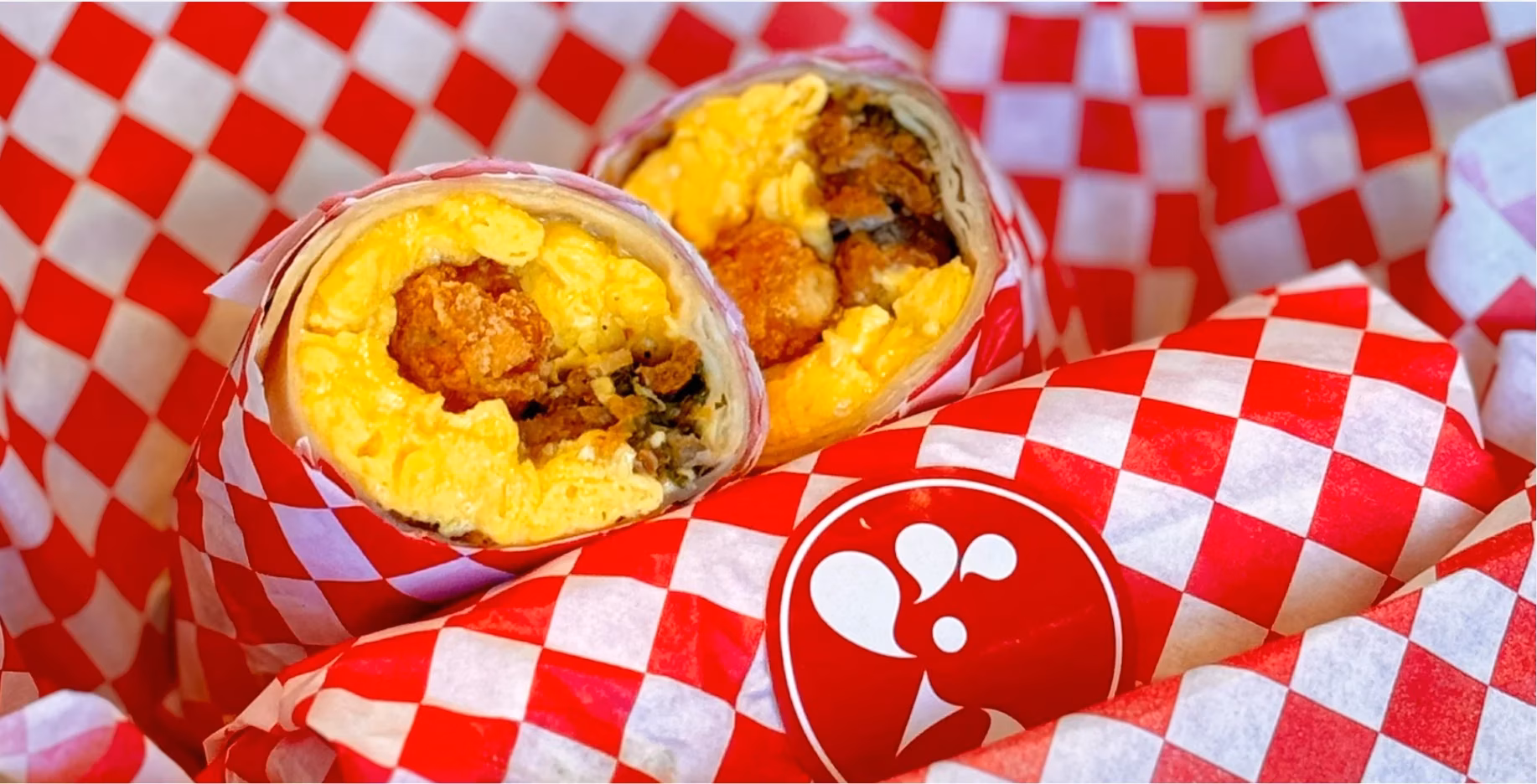 Two burritos filled with eggs and crispy nuggets, wrapped in red checkered paper.
