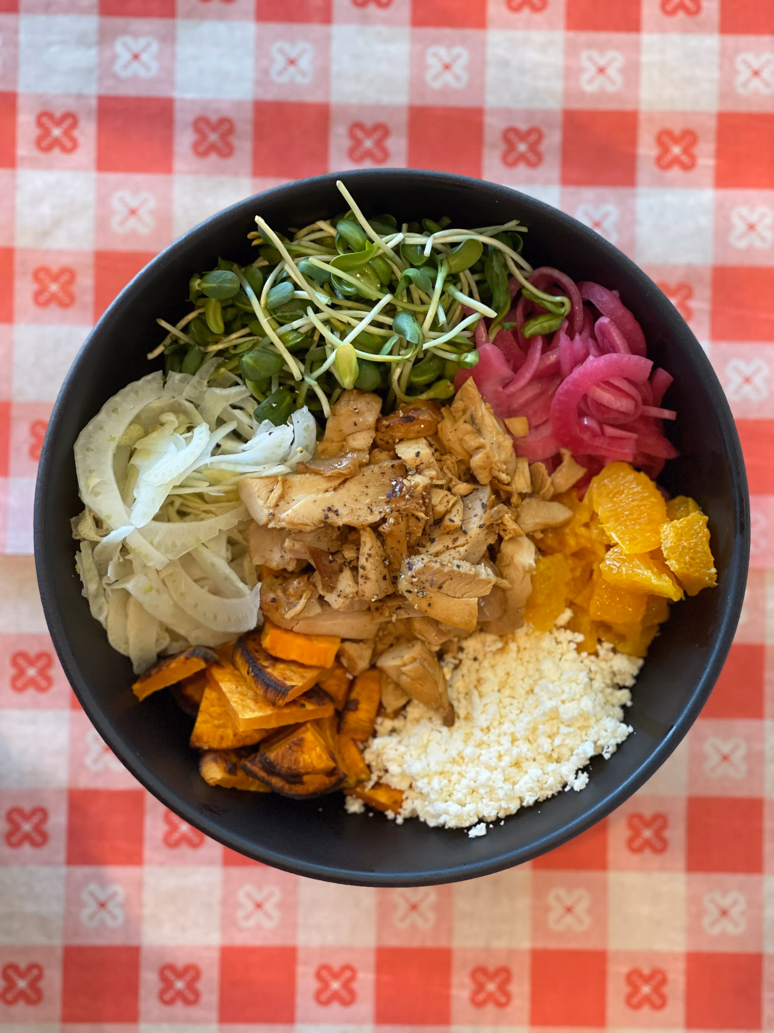 Bowl with chicken, microgreens, pickled onions, cheese, vegetables, and orange.