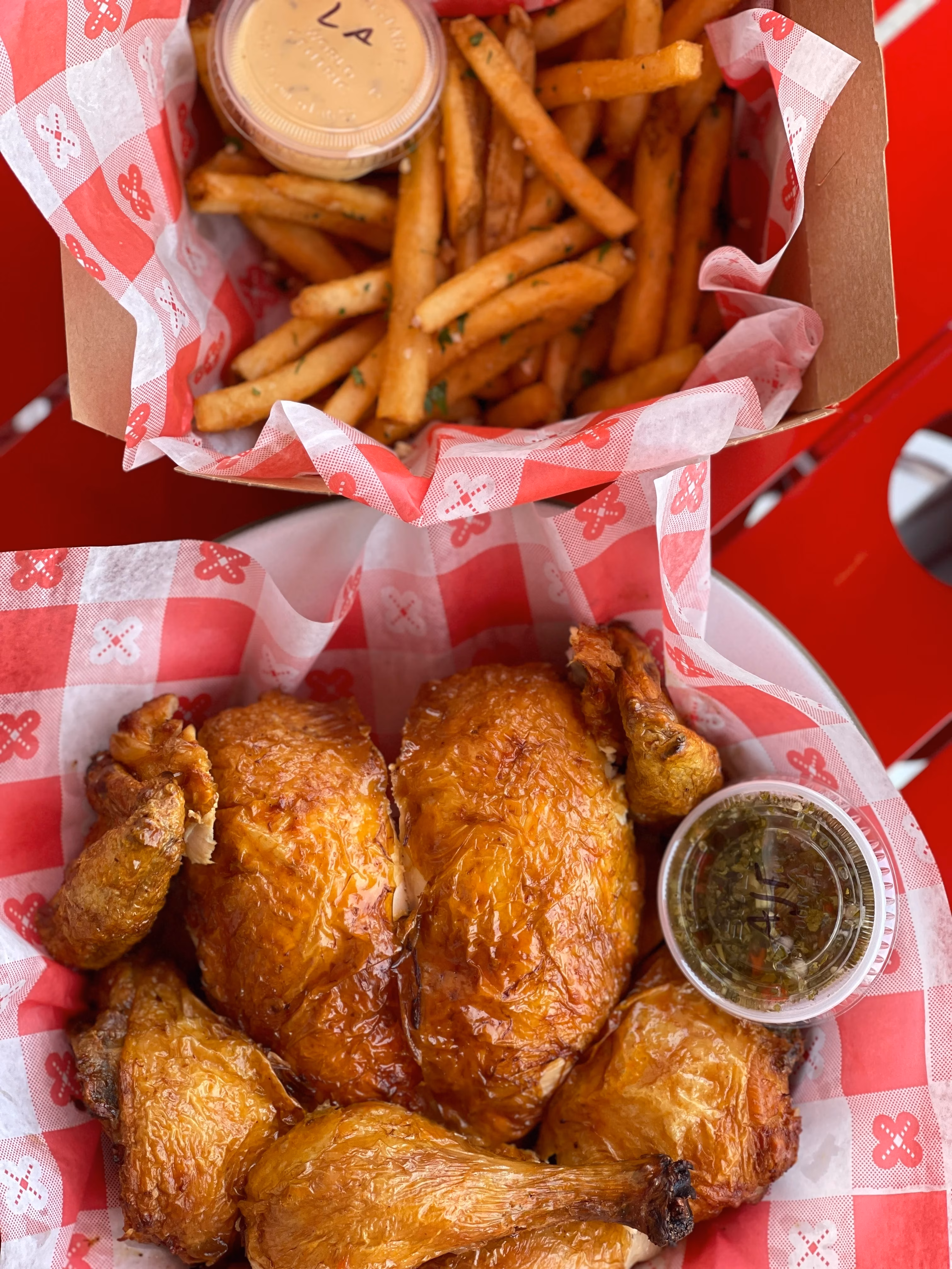 Roasted chicken and french fries with dipping sauces in checkered paper.