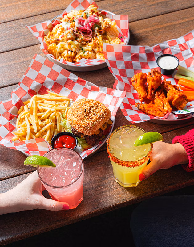 Table with burger, fries, wings, loaded waffle fries, and two drinks.