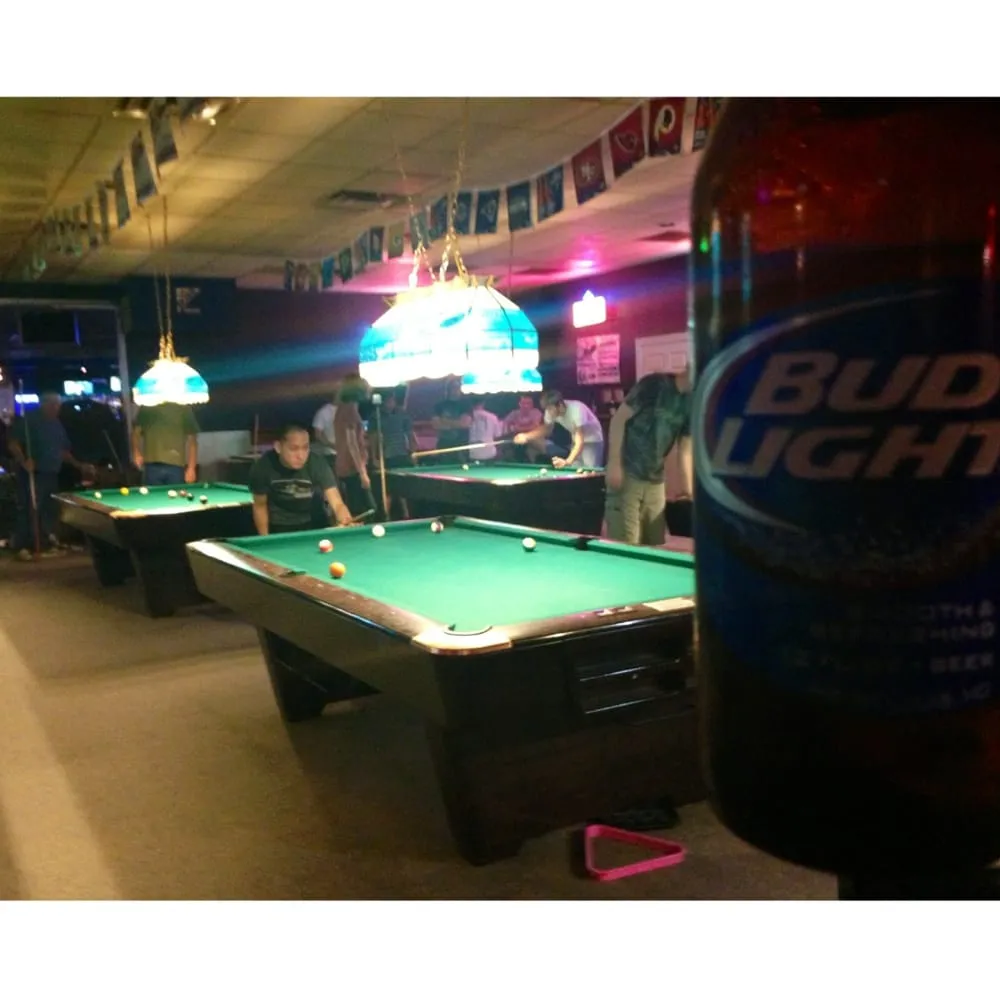 Blurred Bud Light bottle, people playing pool in a hall.
