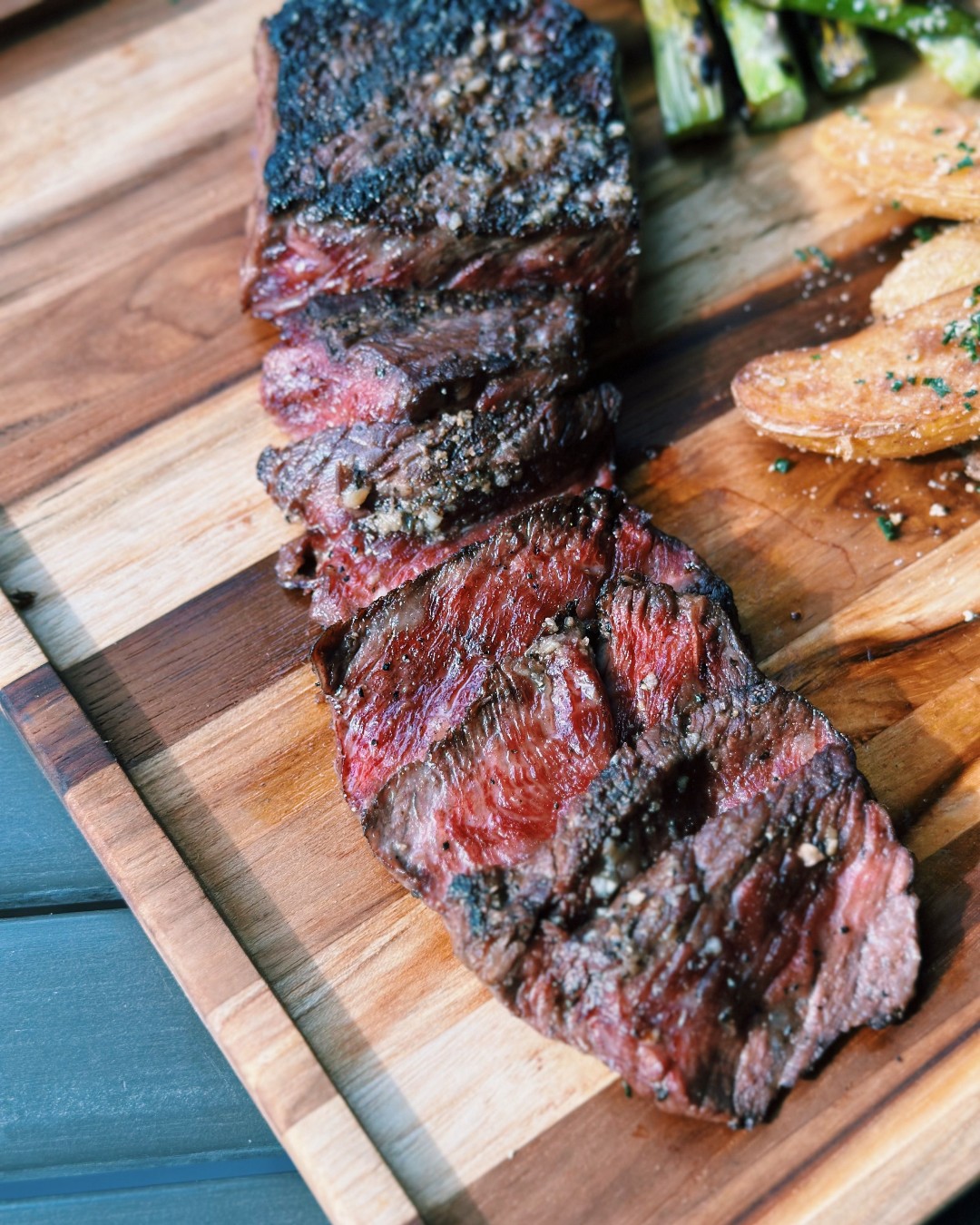 Sliced medium-rare steak with potatoes and asparagus on a wooden board.