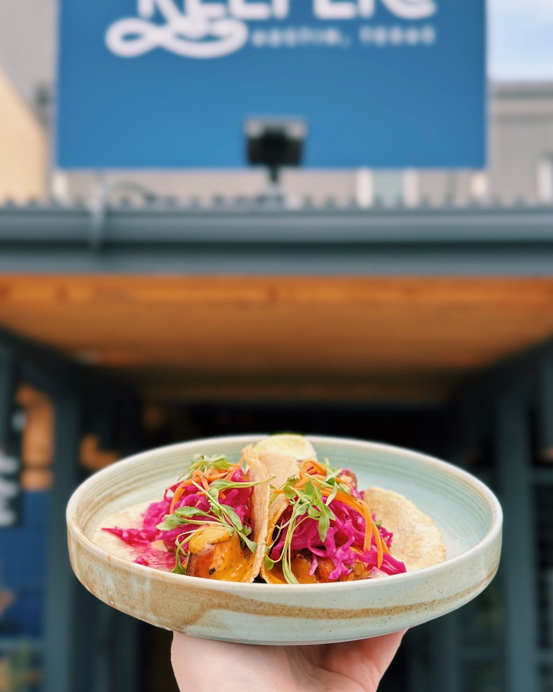 Hand holding a plate of two tacos with red cabbage and greens.