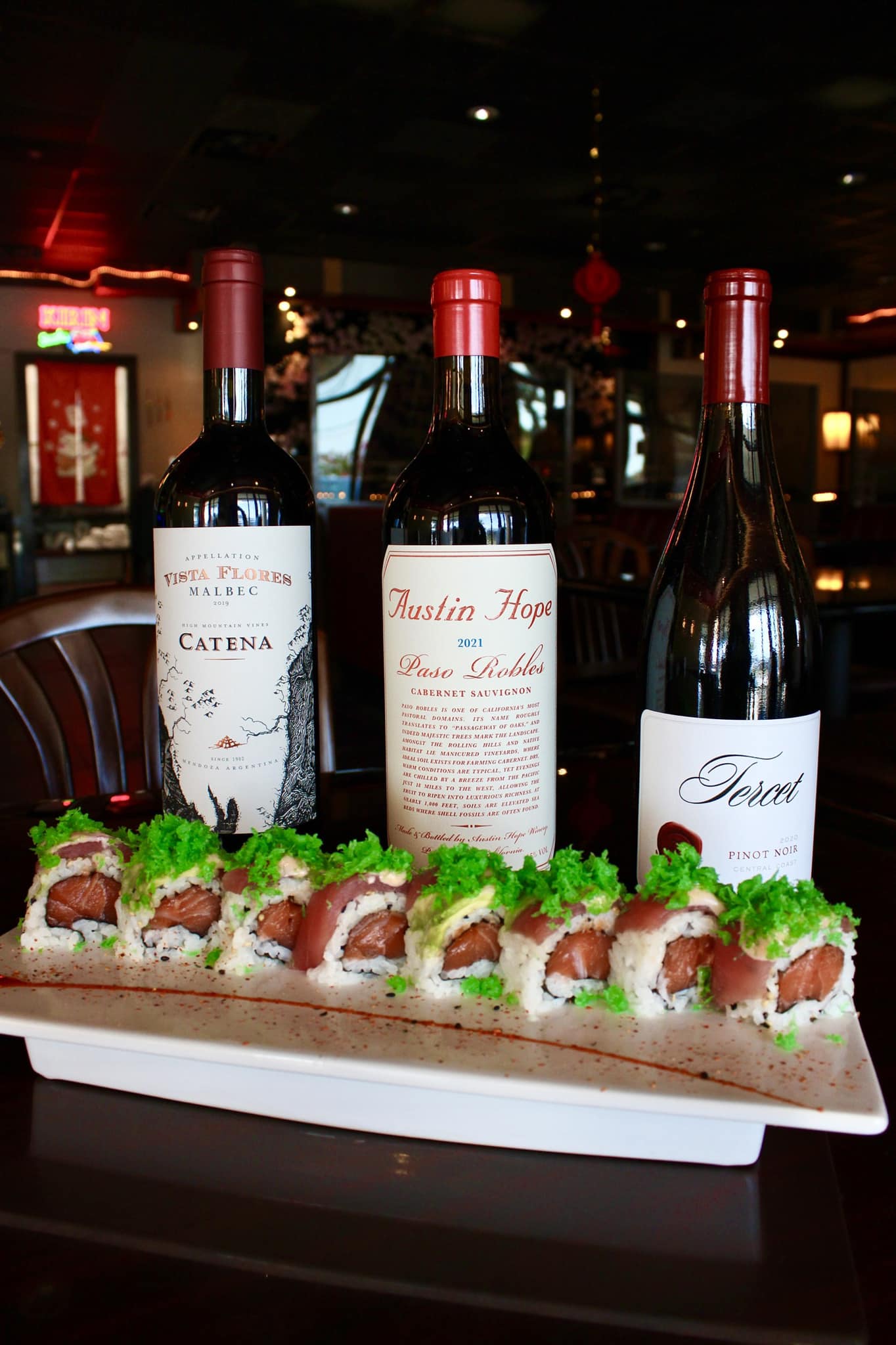 Three red wine bottles and sushi rolls on a platter.