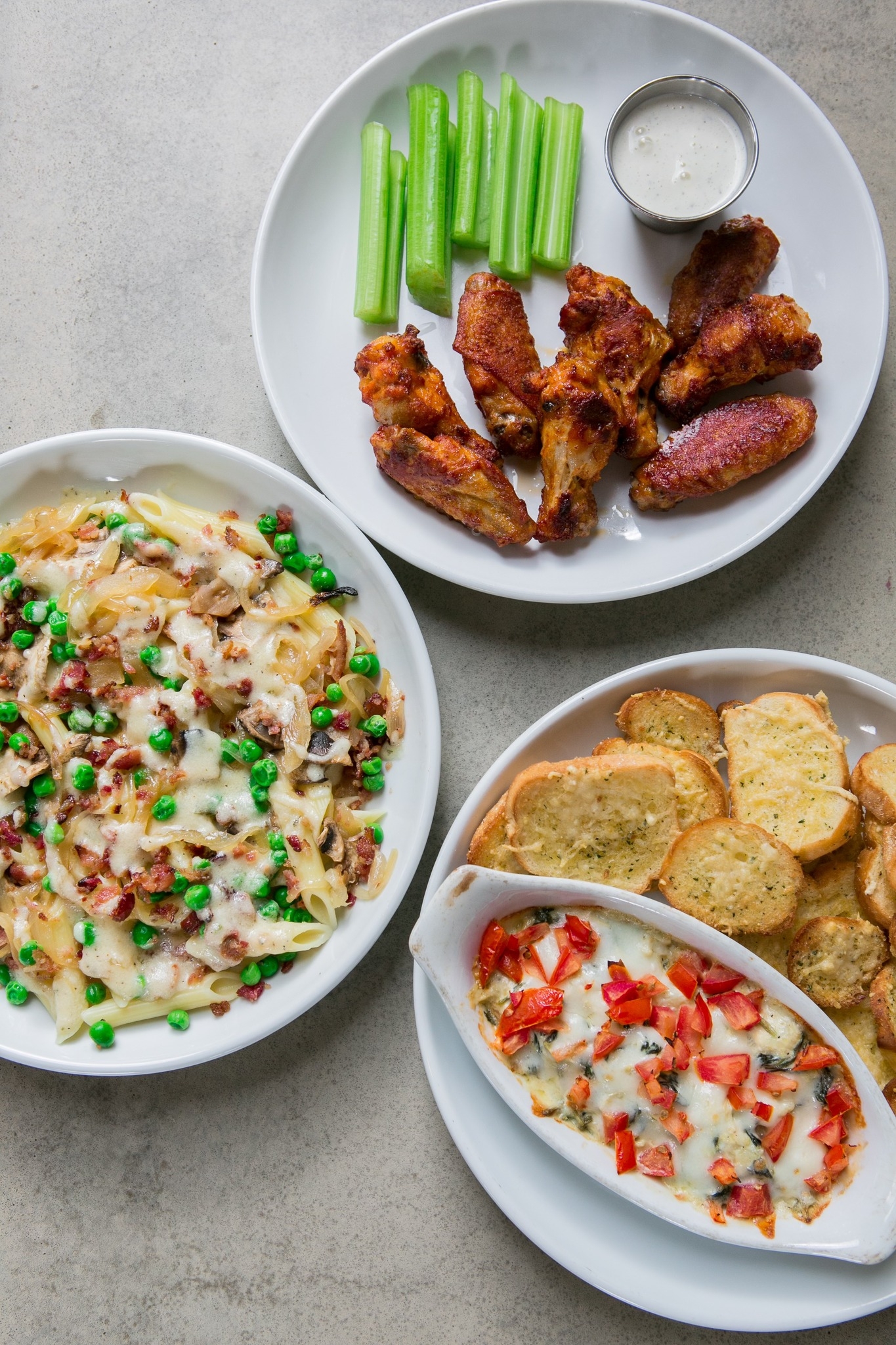 Chicken wings, penne pasta, garlic bread, and hot cheese dip on plates.