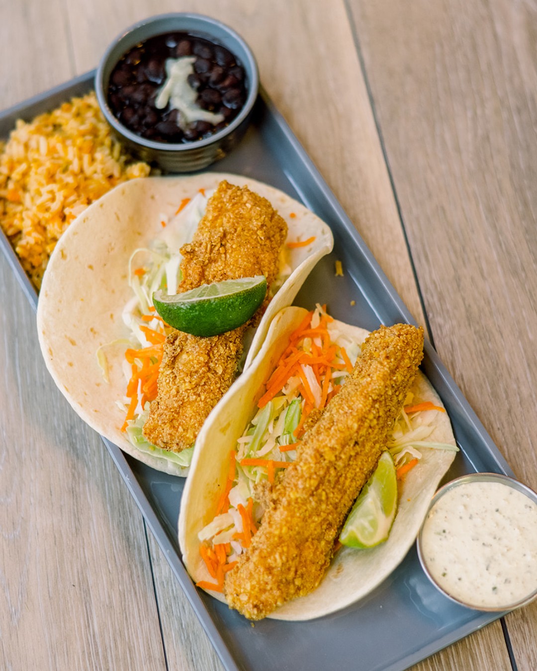 Two crispy fish tacos with rice, black beans, and dipping sauce.