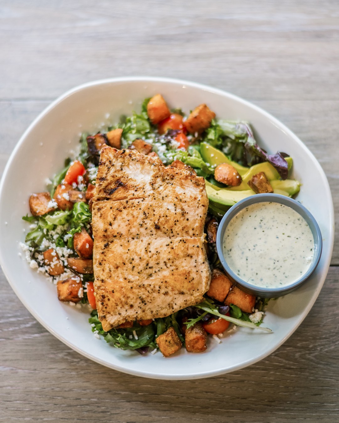 Grilled salmon on a salad with sweet potatoes, avocado, and dressing.