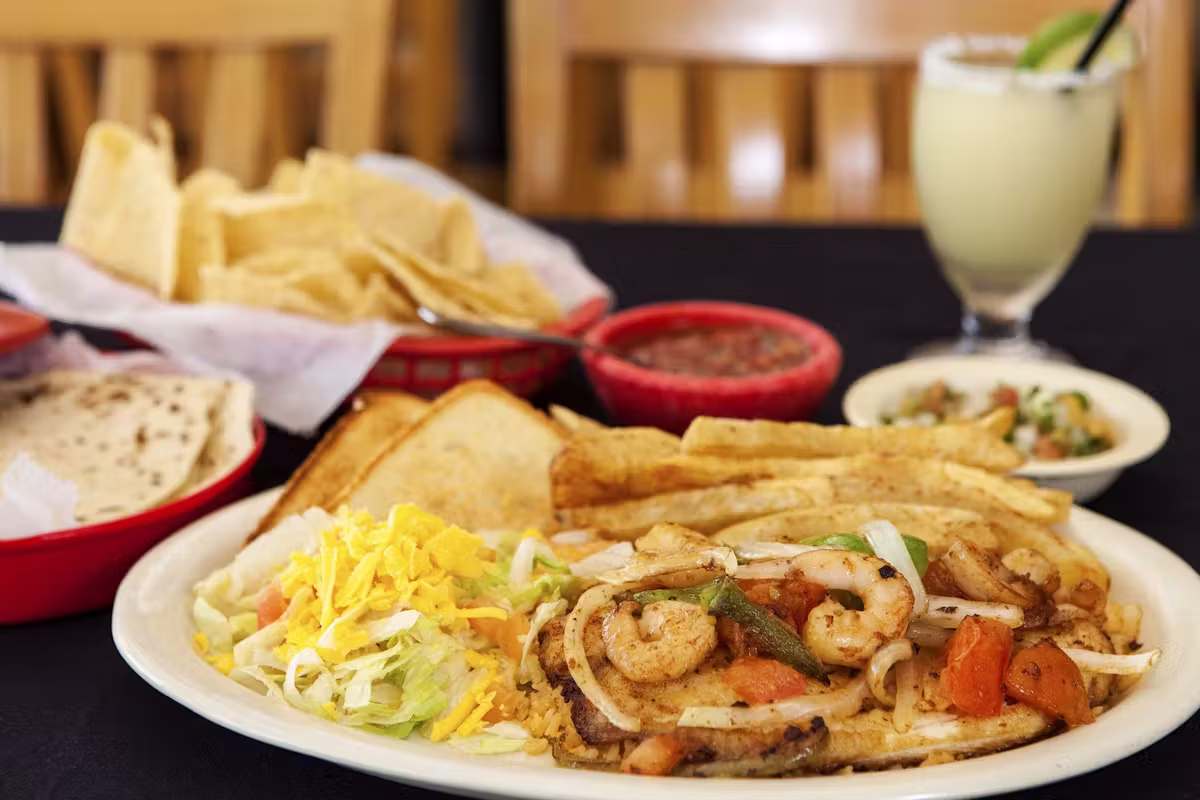 A Mexican meal with fajitas, fries, salad, chips, salsa, and margarita.
