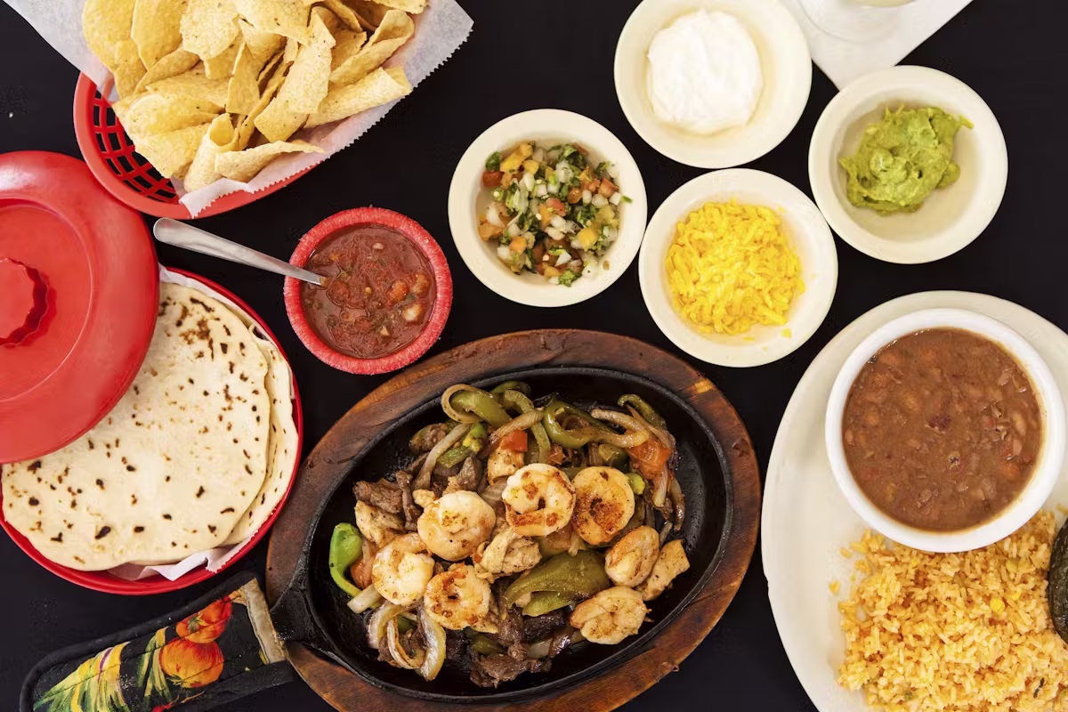 Overhead view of shrimp and steak fajitas with tortillas and side dishes.