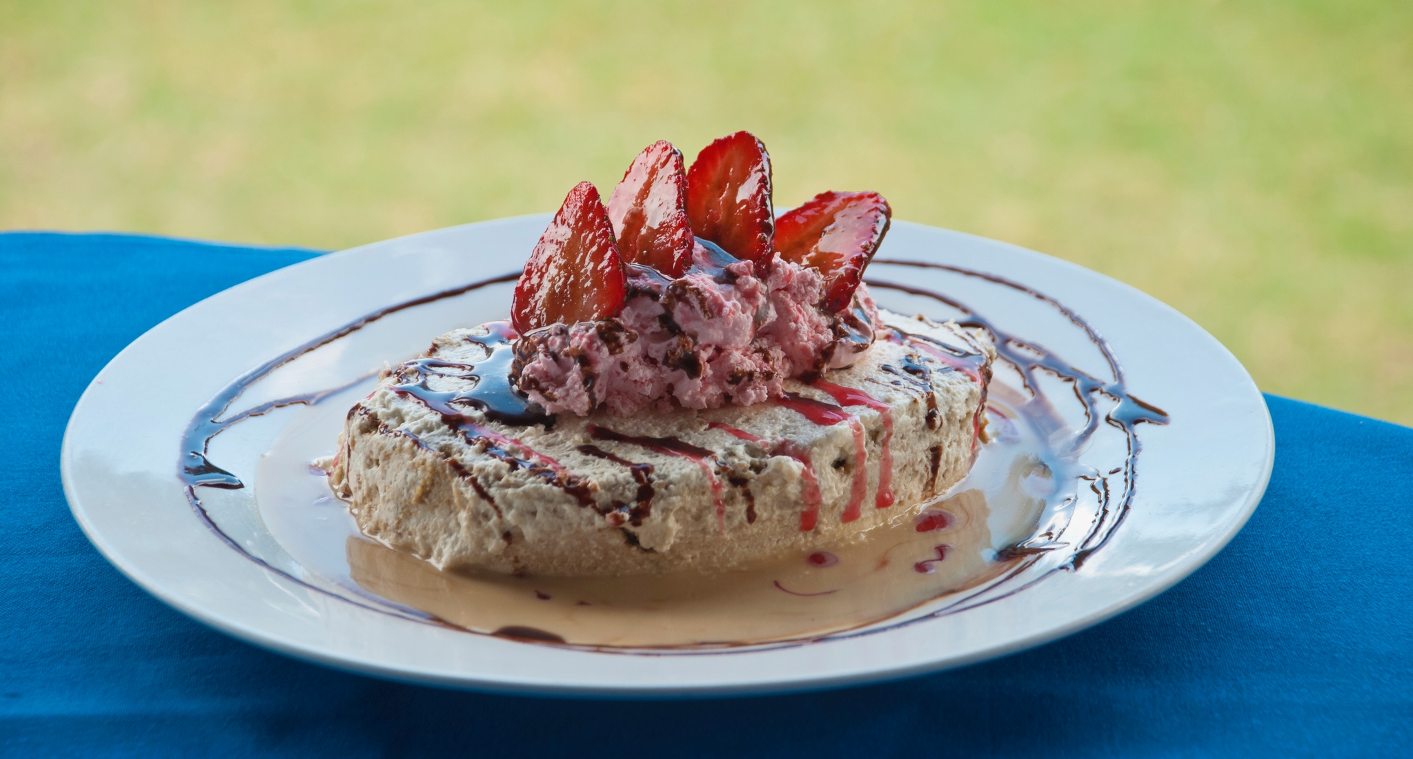 Dessert topped with sliced strawberries, pink cream, and chocolate drizzle.