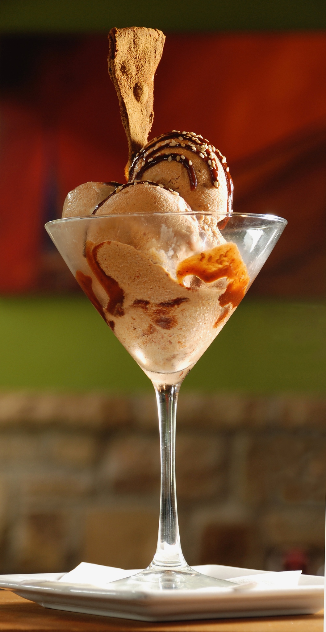 Martini glass with ice cream, chocolate drizzle, sesame seeds, and a cookie.