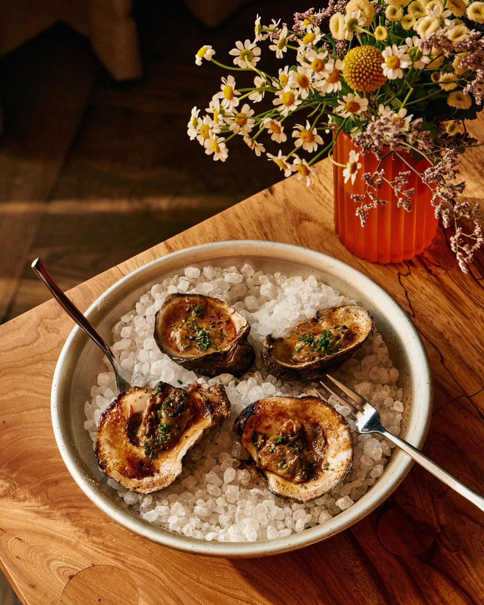 Four cooked oysters on crushed ice, garnished with chives and flowers.