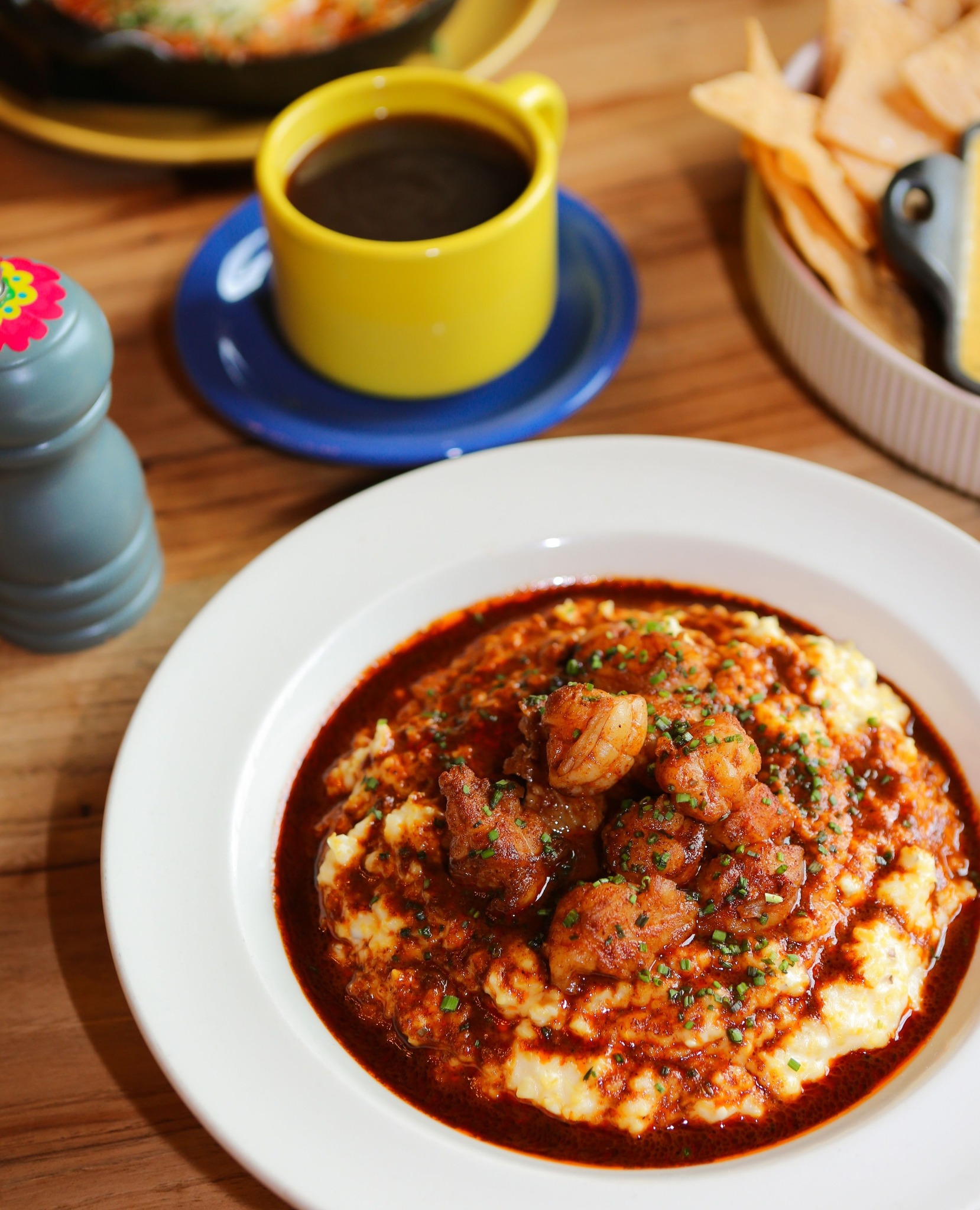 Shrimp and grits with red sauce and chives, coffee, chips.