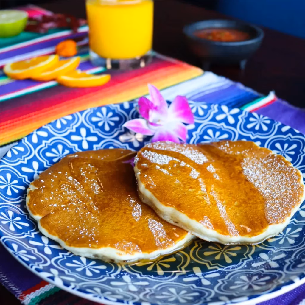 Pancakes with syrup, powdered sugar, and orchid on a colorful table.