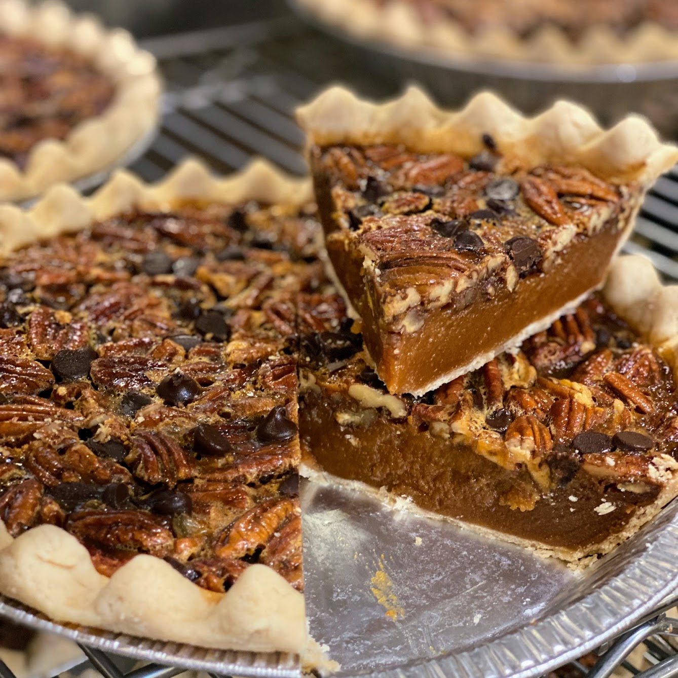 A whole chocolate chip pecan pie with a slice on top.