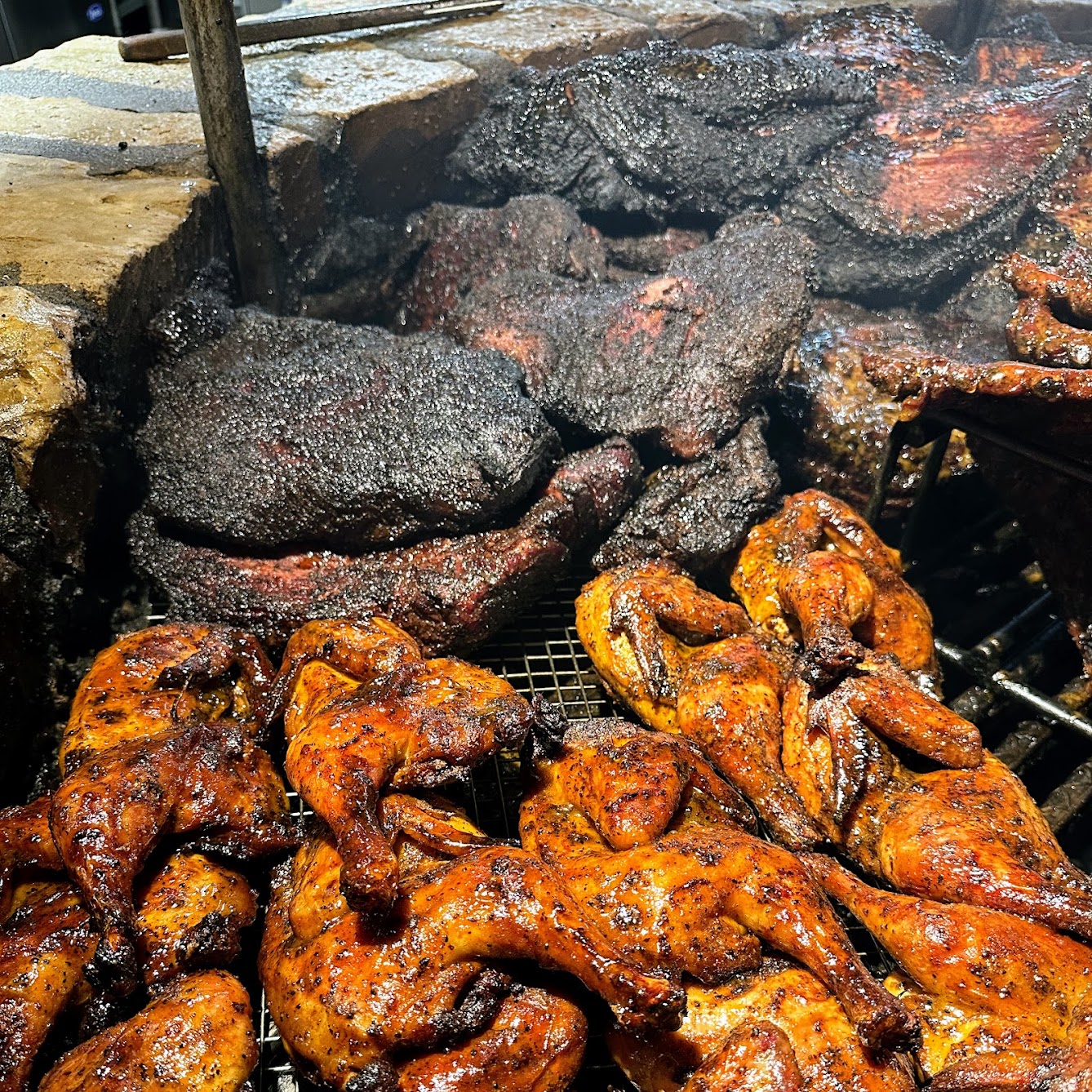 Rows of barbecued chicken and dark smoked meats in a large pit.