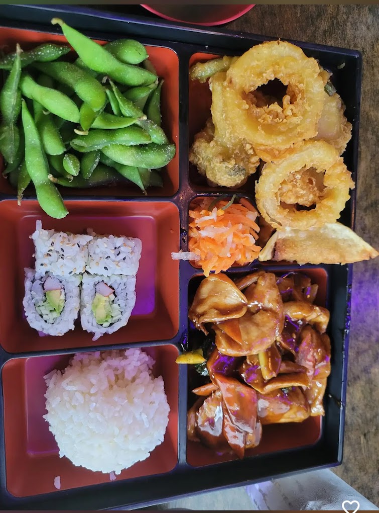 A bento box containing edamame, sushi, tempura, rice, and chicken stir-fry.