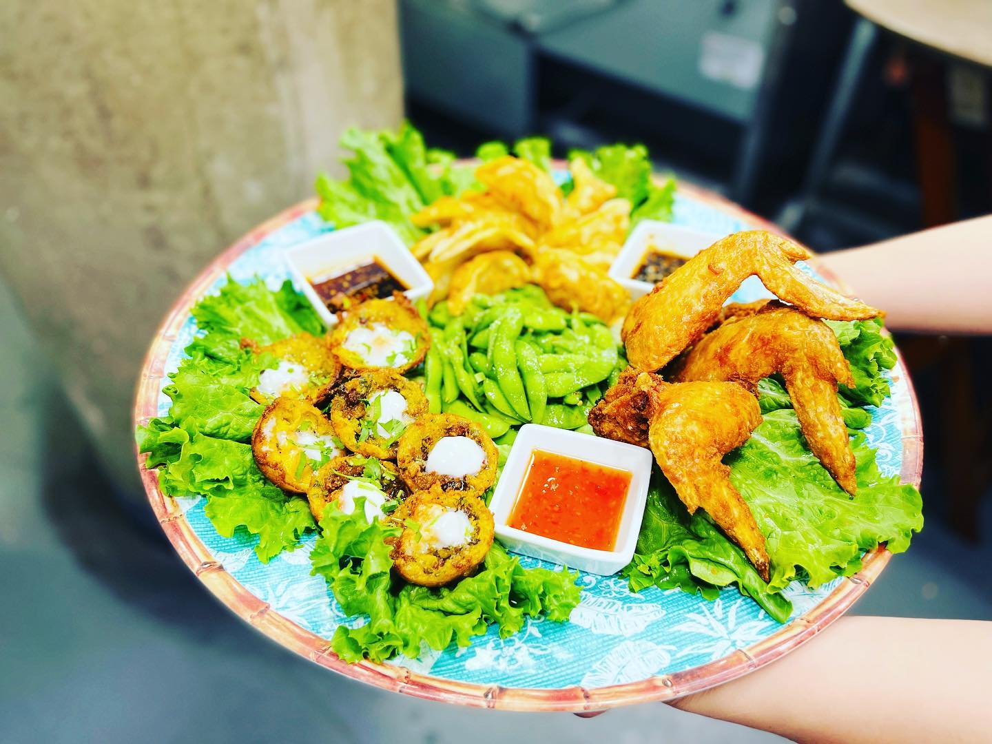 Platter with fried chicken, assorted appetizers, green vegetables, and sauces.