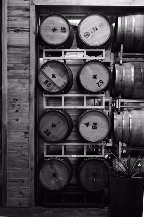 Black and white image of wine barrels stacked on metal racks.