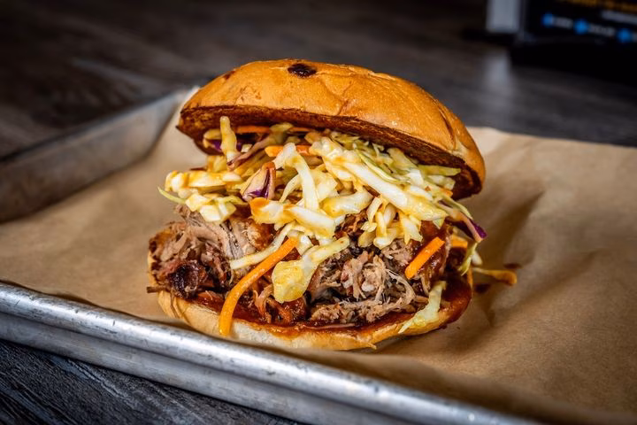 Pulled pork sandwich with coleslaw on a bun, served on a tray.