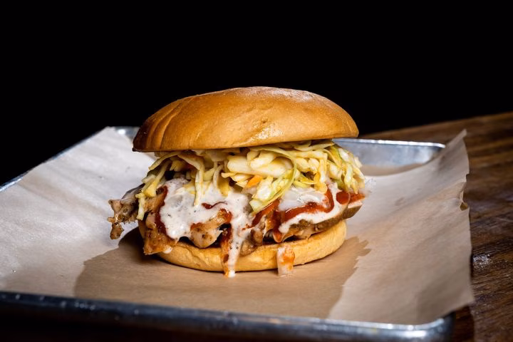 Shredded meat sandwich with coleslaw and two sauces on a tray.