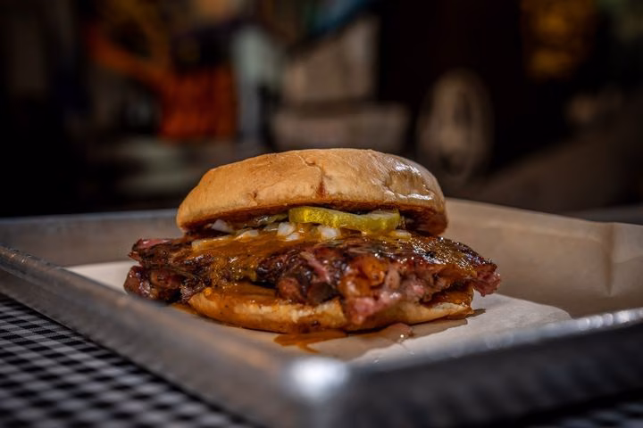 Barbecue meat sandwich with pickles and sauce on a metal tray.