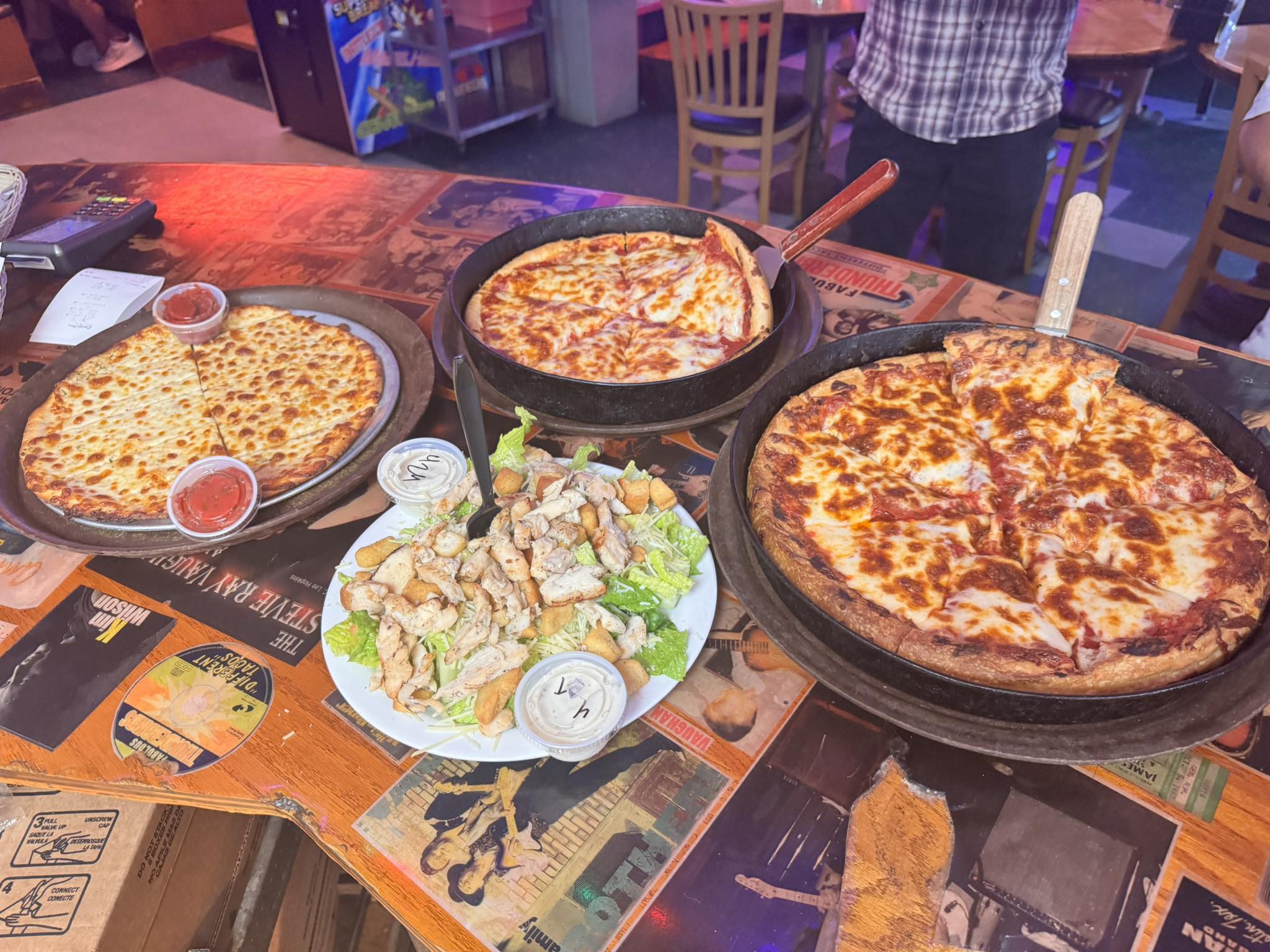 Three cheese pizzas and a chicken Caesar salad on a table.
