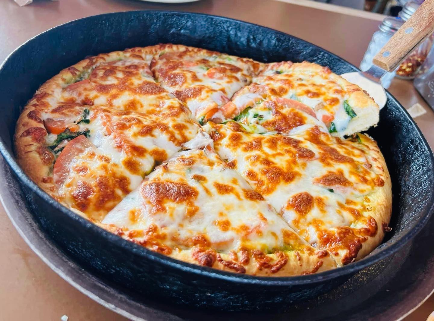 Deep-dish pizza with melted cheese, tomatoes, and greens in a pan.