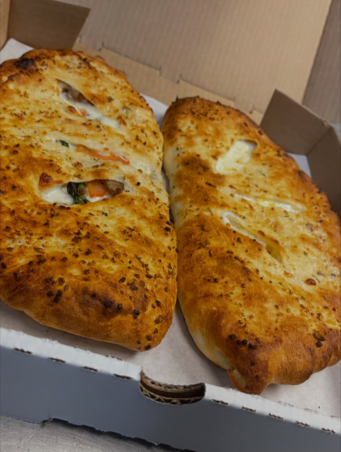 Two golden-brown calzones with visible cheese and vegetable filling in a box.