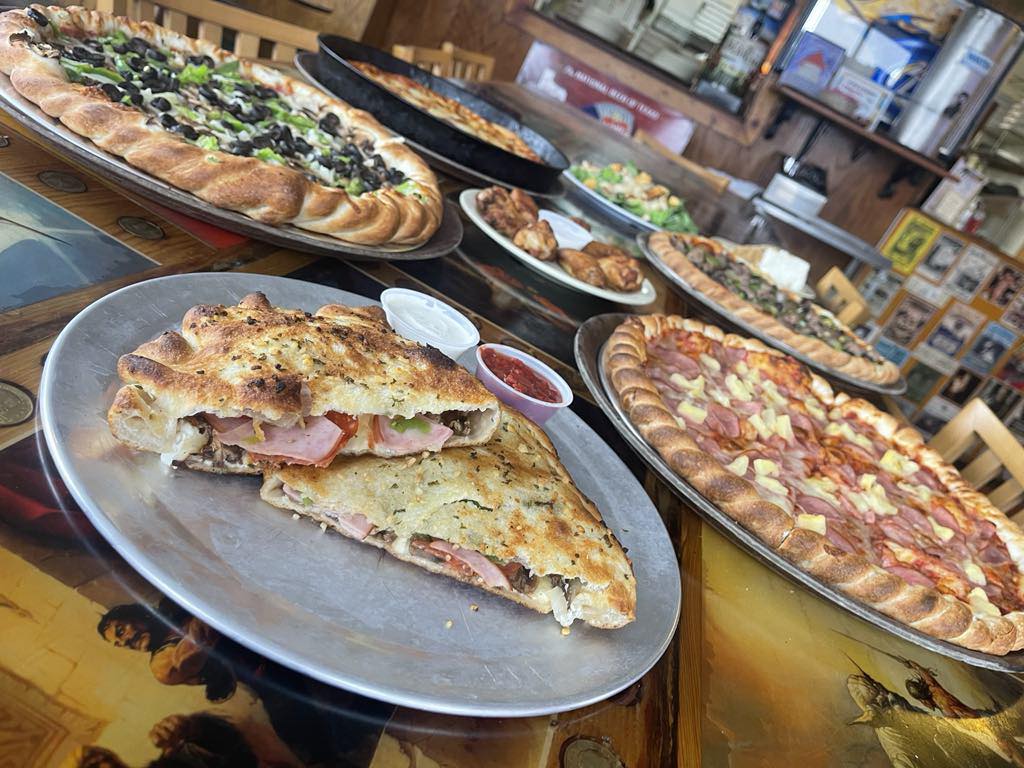 Sliced calzone and assorted pizzas, including Hawaiian, on restaurant tables.