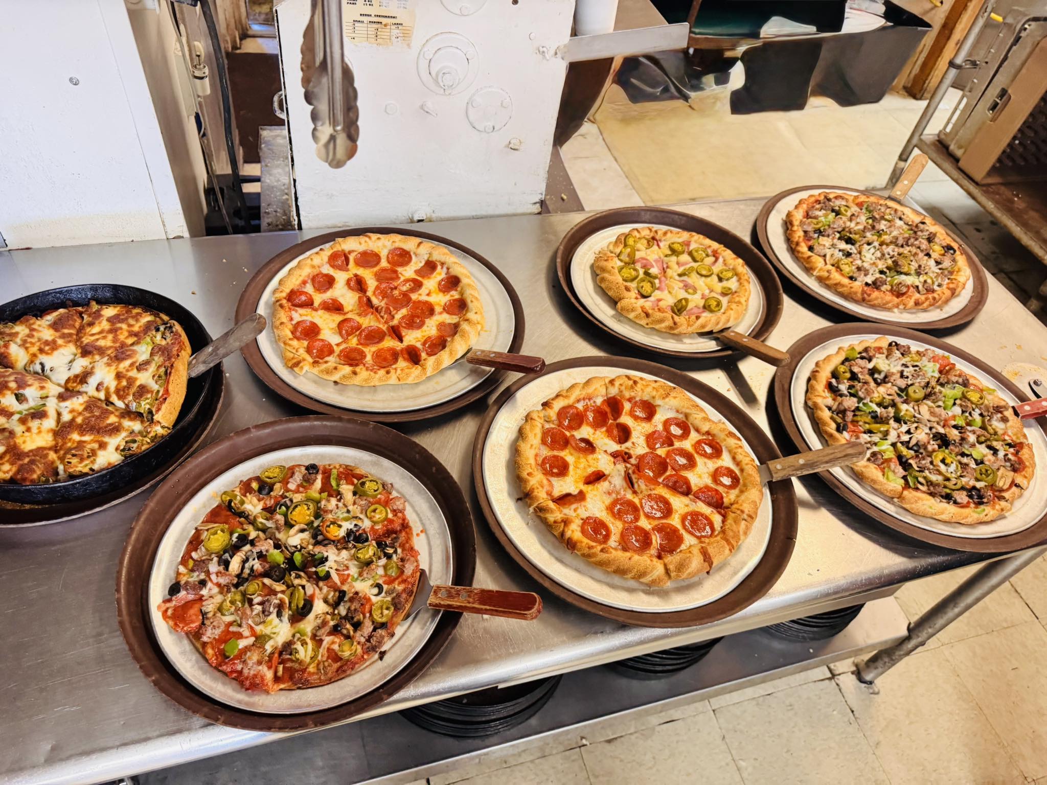 Several pizzas with diverse toppings on a metal counter.