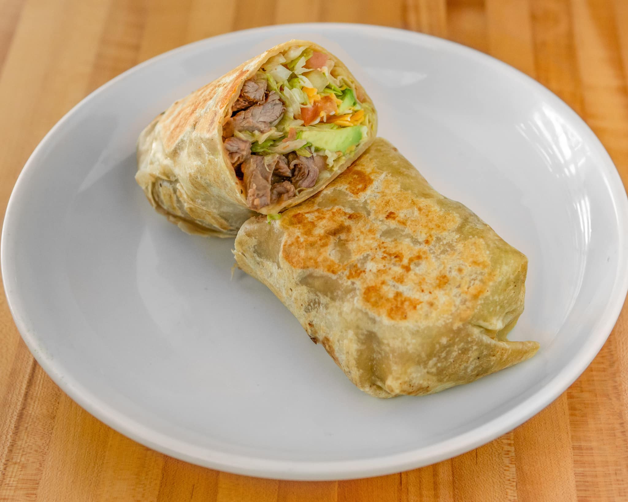 Steak burrito cut open with lettuce, avocado, cheese, and tomato.