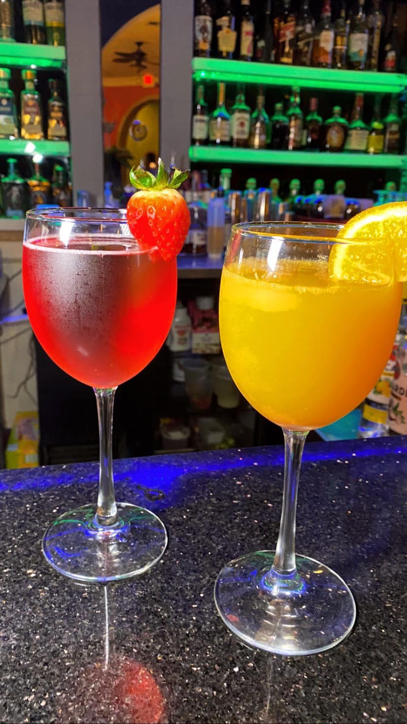 Two cocktails, one red with strawberry, one orange with orange slice.