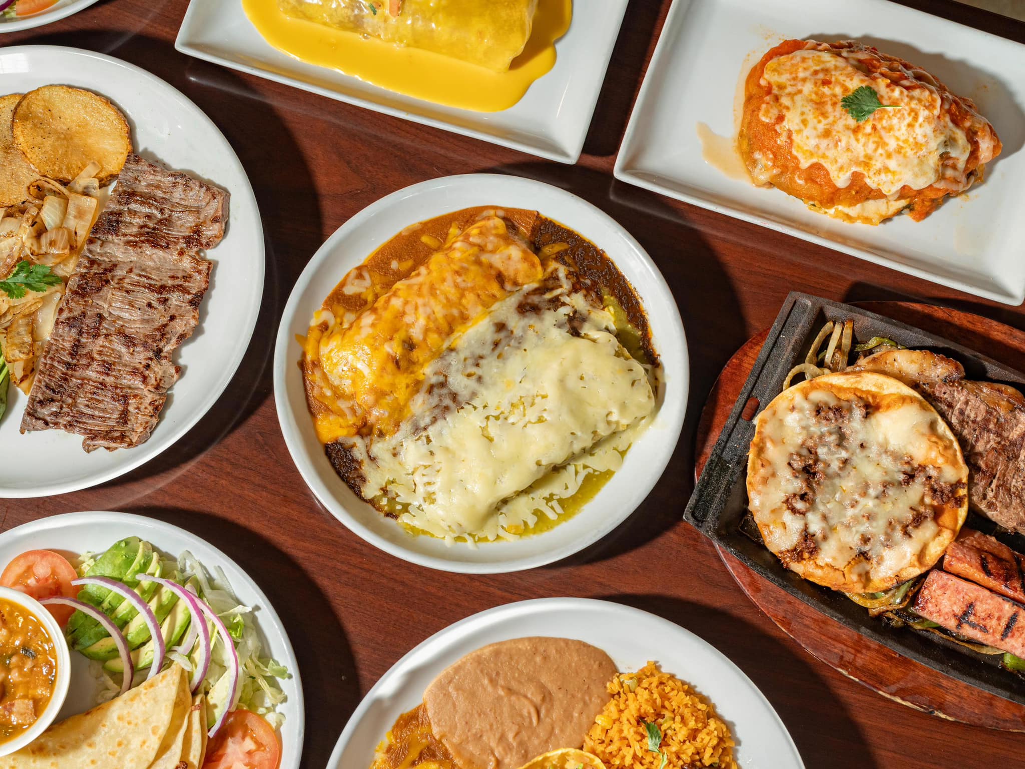 An overhead view of multiple plates of Mexican food on a wooden table.