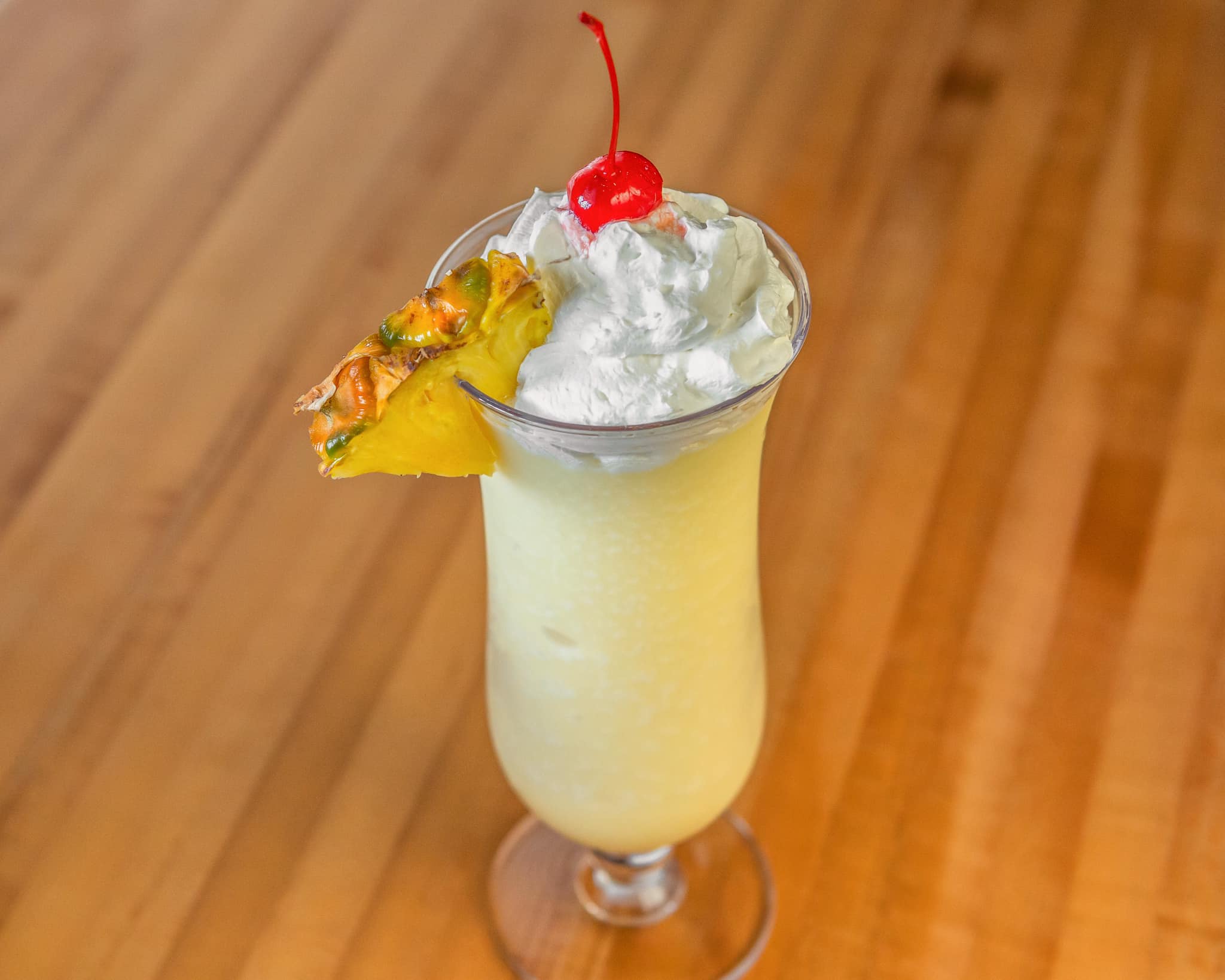Yellow frozen drink with whipped cream, cherry, and pineapple garnish.